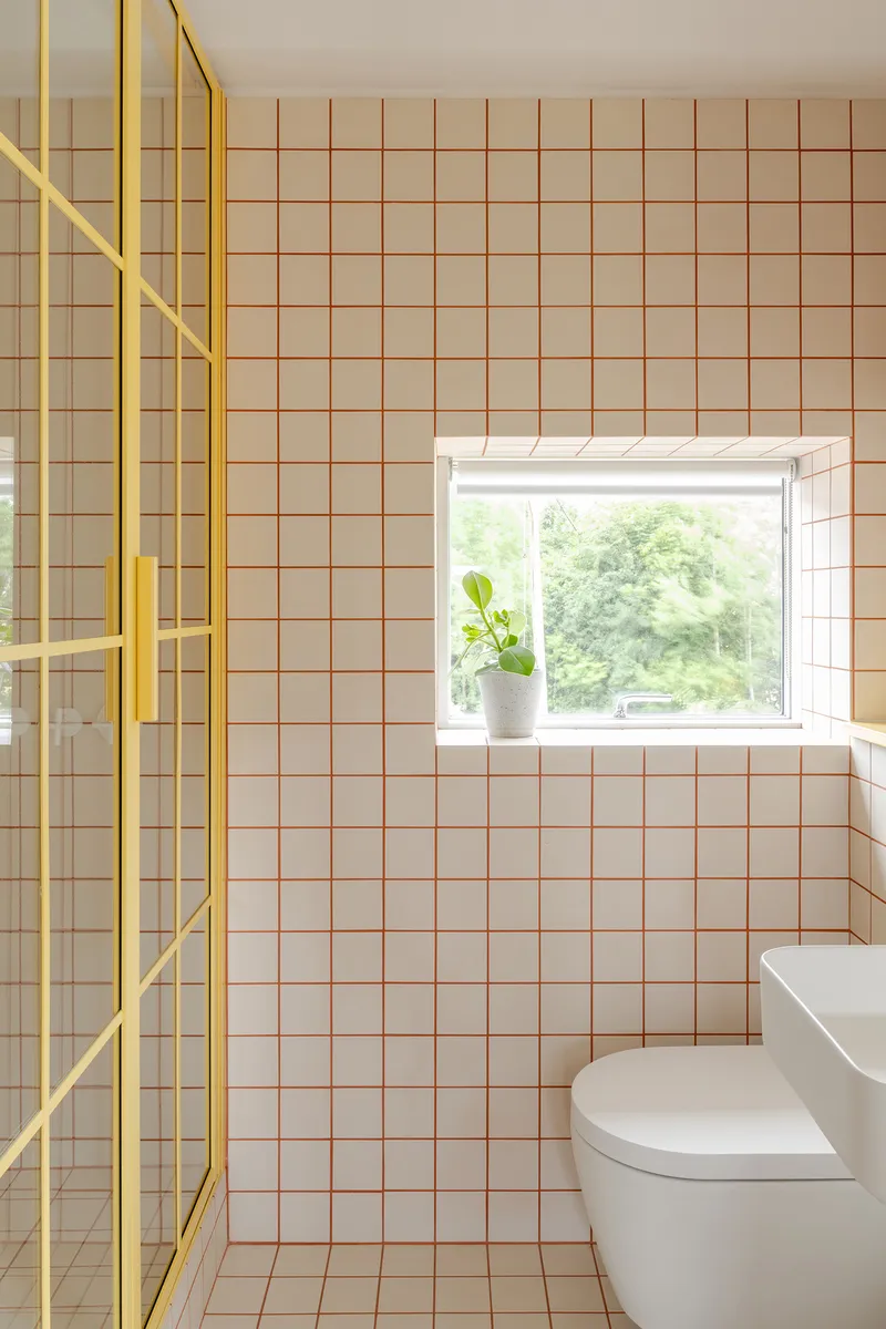 Bathroom corner with pink square tiles, yellow shower partition, and window with potted plant