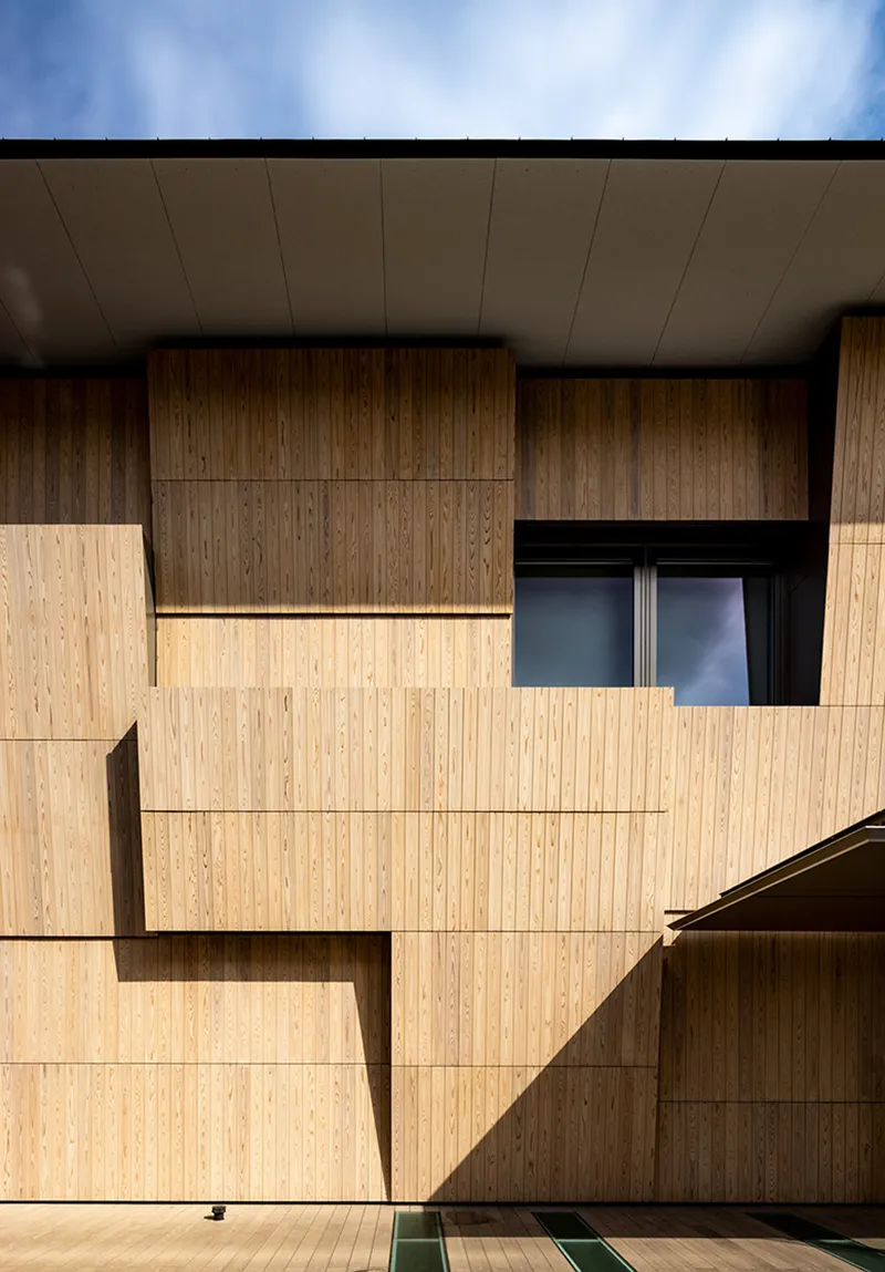 Stacked timber panels creating shadow play on facade under deep eaves