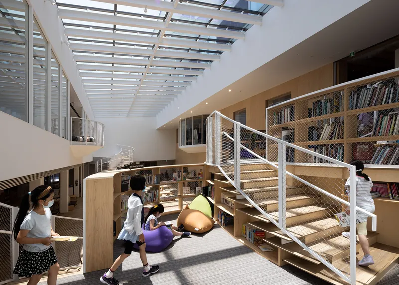Double-height library interior with metal staircase and slatted skylight above