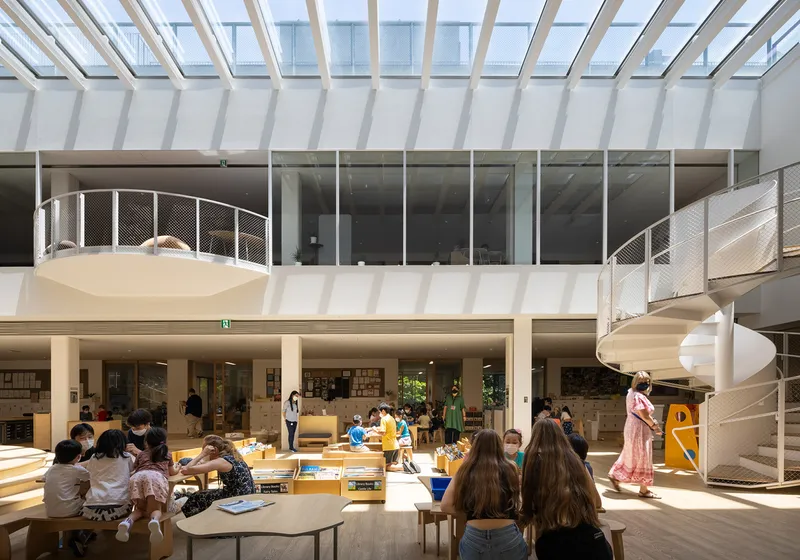 Double-height library atrium with spiral staircase, glazed skylight and children seated at low tables