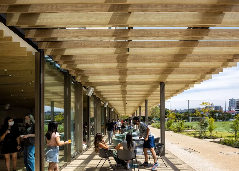 Covered exterior walkway with alternating timber ceiling panels and students gathering in afternoon light