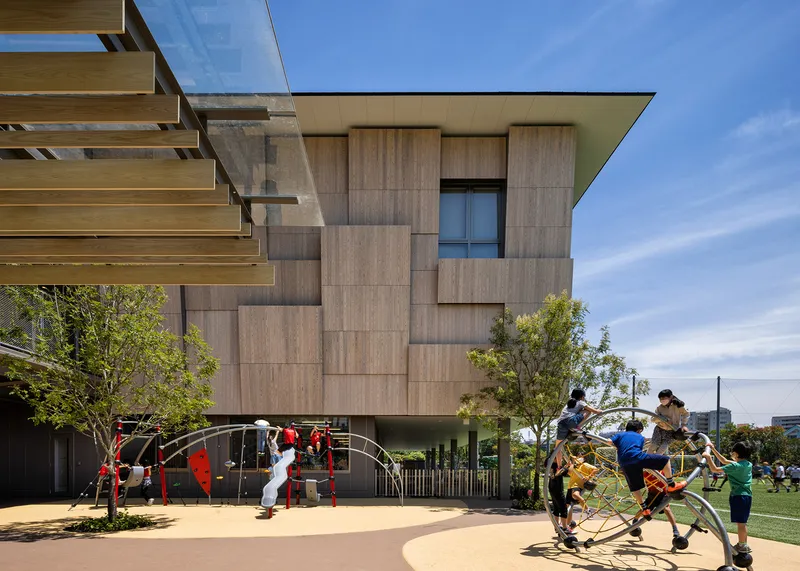 Elevated volume clad in staggered timber panels above a playground with children on climbing equipment