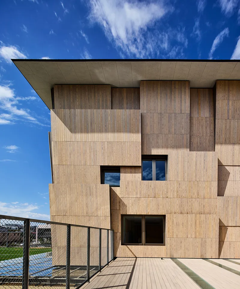 Corner detail of the offset timber cladding system with recessed windows under clear afternoon sun