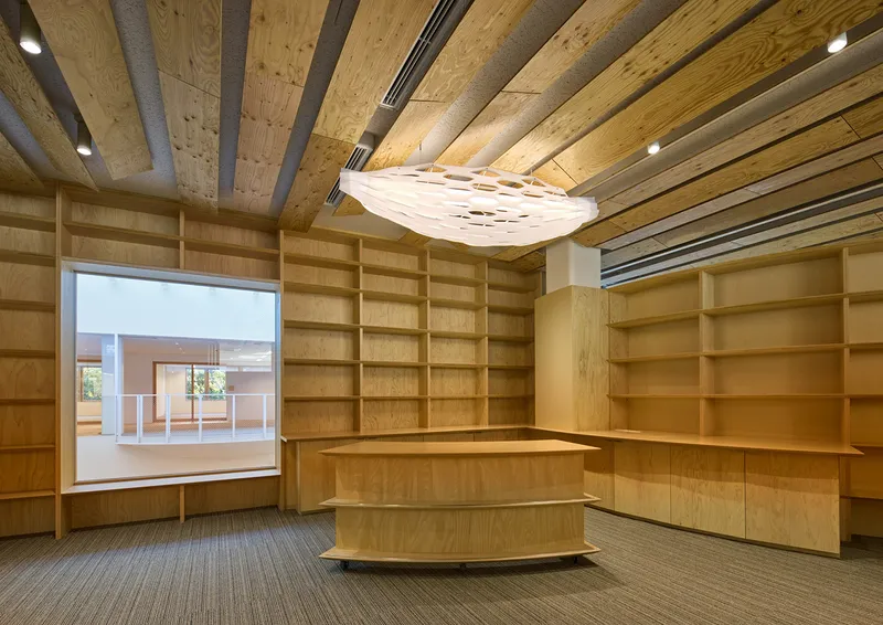 Plywood-lined reading room with floor-to-ceiling shelving, central service desk and exposed timber ceiling beams