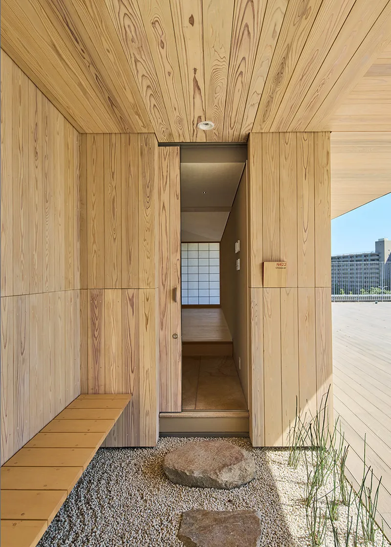 Timber-clad entrance courtyard with gravel garden, stepping stones and wooden bench under a slatted ceiling