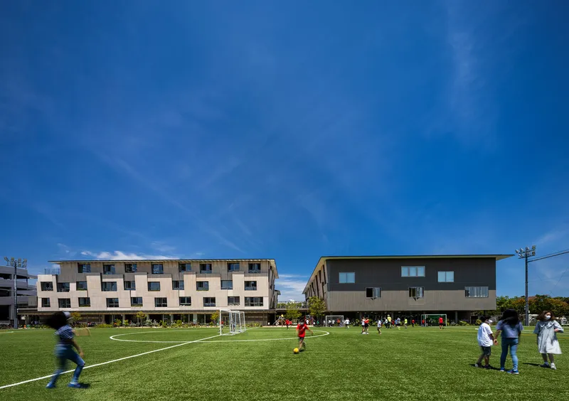 Two residential blocks flanking a sports field with children playing soccer on synthetic turf