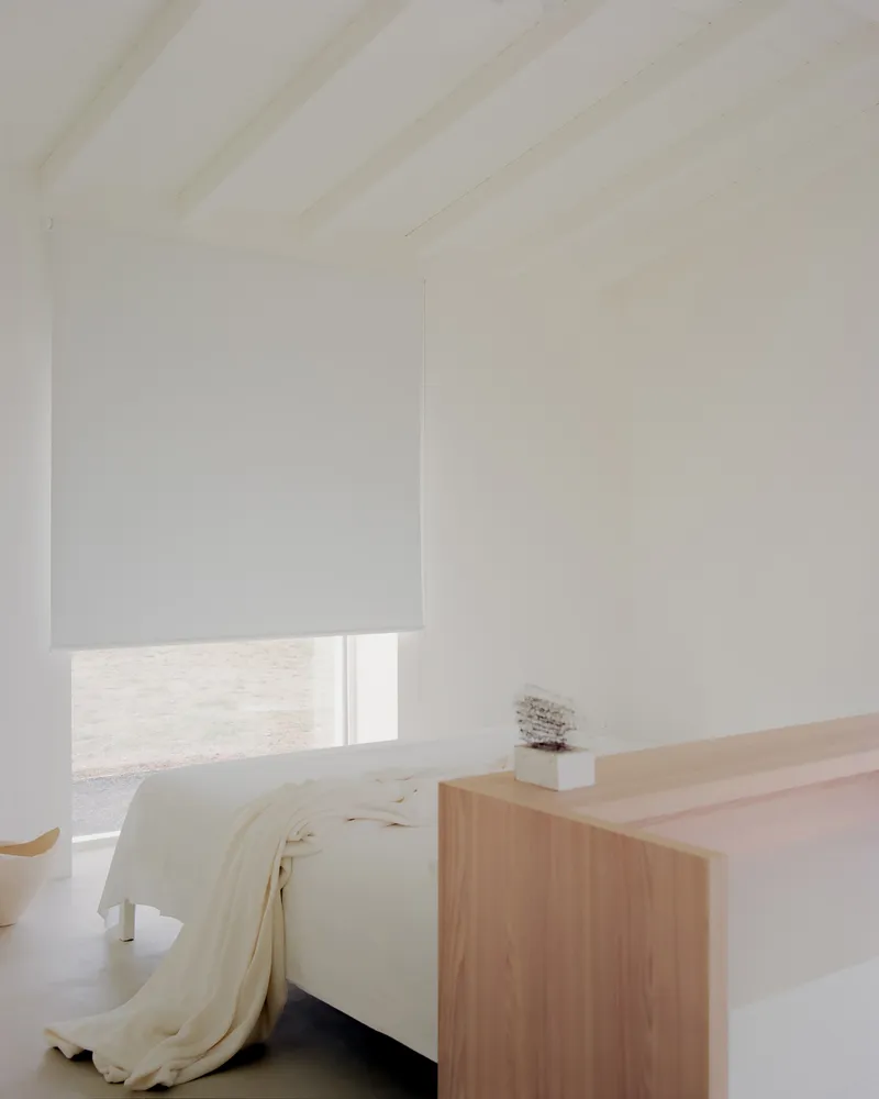 Bedroom with a pale timber headboard wall and a window fitted with a white roller shade