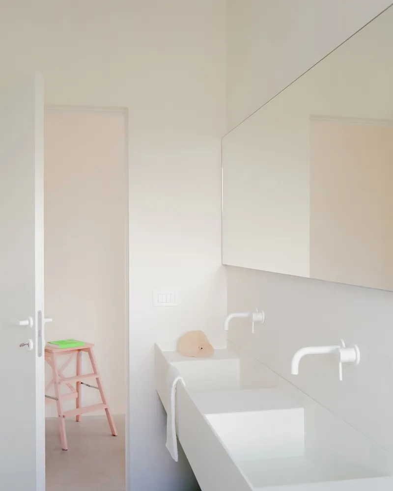 Bathroom with white wall-mounted sinks, mirrors, and a pink stepstool visible through the doorway