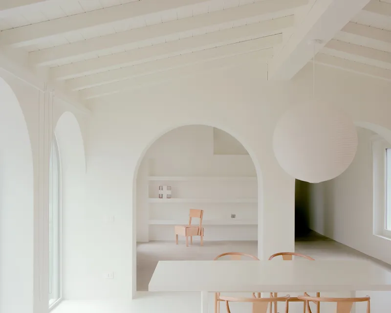 White interior with arched openings connecting dining and living spaces under exposed timber ceiling