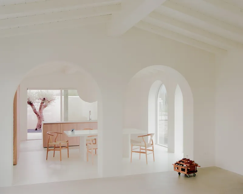 View through arched doorway to kitchen with light wood cabinetry and dining chairs
