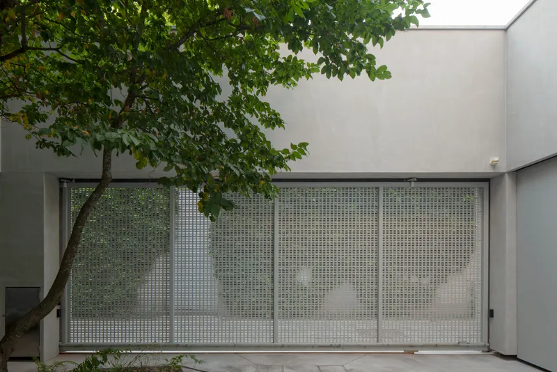 Perforated metal gate beneath tree canopy framed by rendered concrete walls