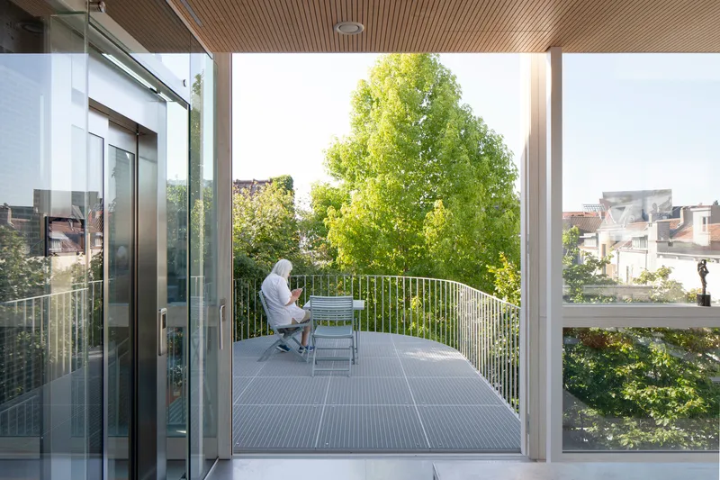 Covered terrace with slatted timber ceiling where a person sits reading beside tree