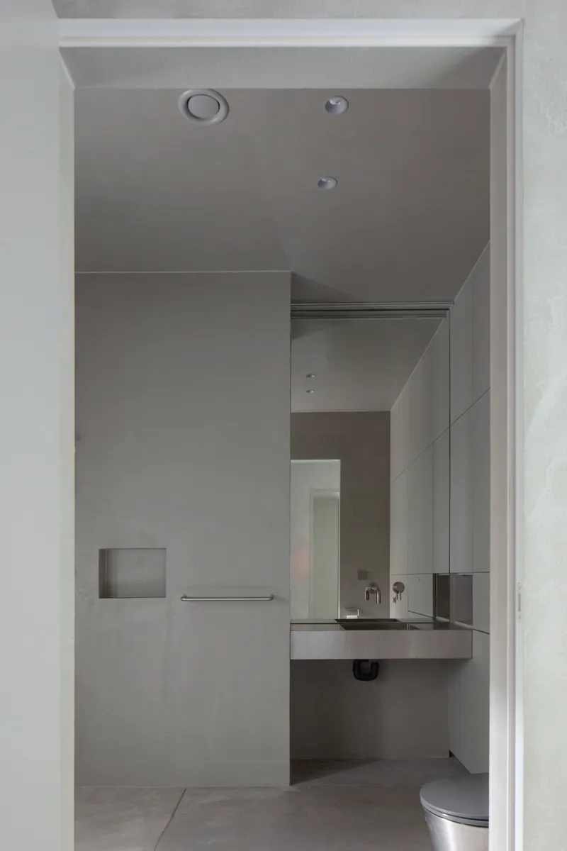 Compact bathroom with floating concrete sink and recessed niche seen through a white doorway