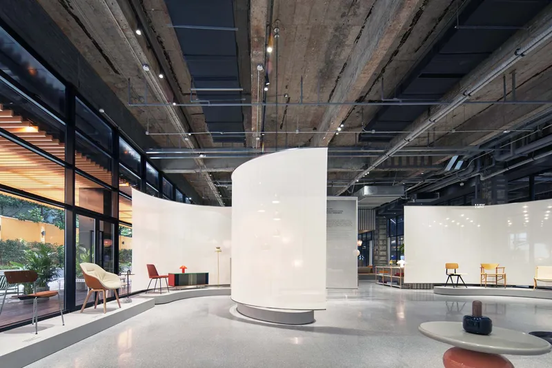 Curved white partition wall in open interior with exposed concrete ceiling and floor-to-ceiling windows