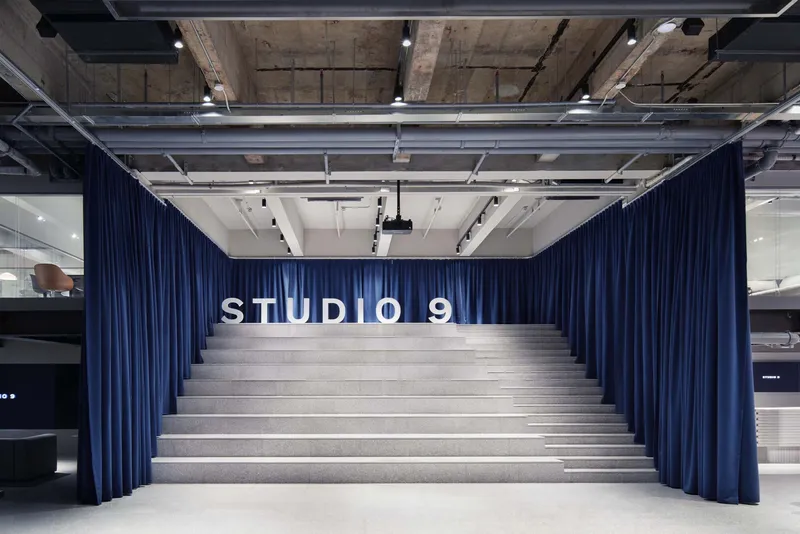 Wide stepped seating area flanked by blue curtains under exposed concrete ceiling with track lighting
