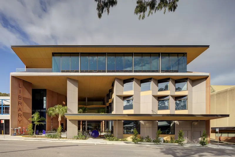 Street view of the cantilevered facade with timber soffits and full-height glazing under cloudy skies