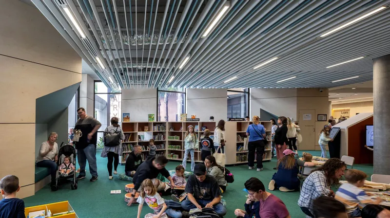 Library space with linear metal ceiling baffles and children seated on green carpet reading