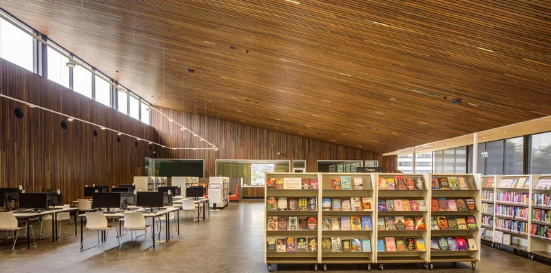 Open library interior with sloped timber ceiling and book display shelving under ribbon windows
