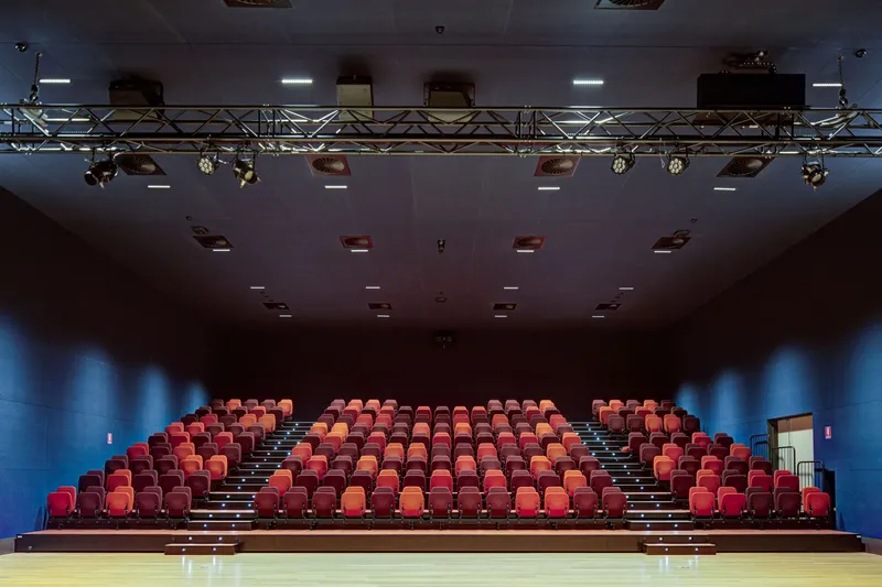 Auditorium seating in red and orange upholstery with theatrical lighting rig overhead