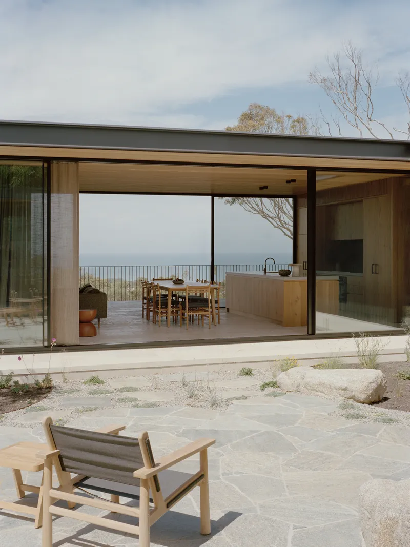 Glass sliding doors opening from courtyard to dining room with ocean horizon visible through opposite glazing