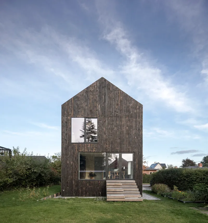 Garden facade with vertical timber cladding, gabled roof and external timber stair under evening sky