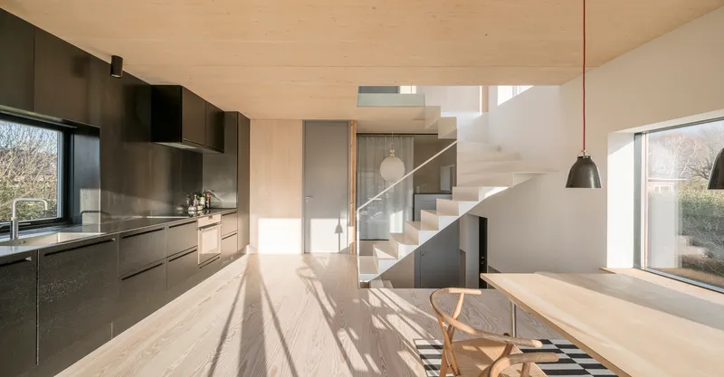 Open-plan kitchen and dining area with plywood ceiling and staircase bathed in afternoon sunlight