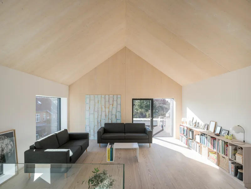 Living room with vaulted plywood ceiling, low bookshelf and framed view to outdoor terrace