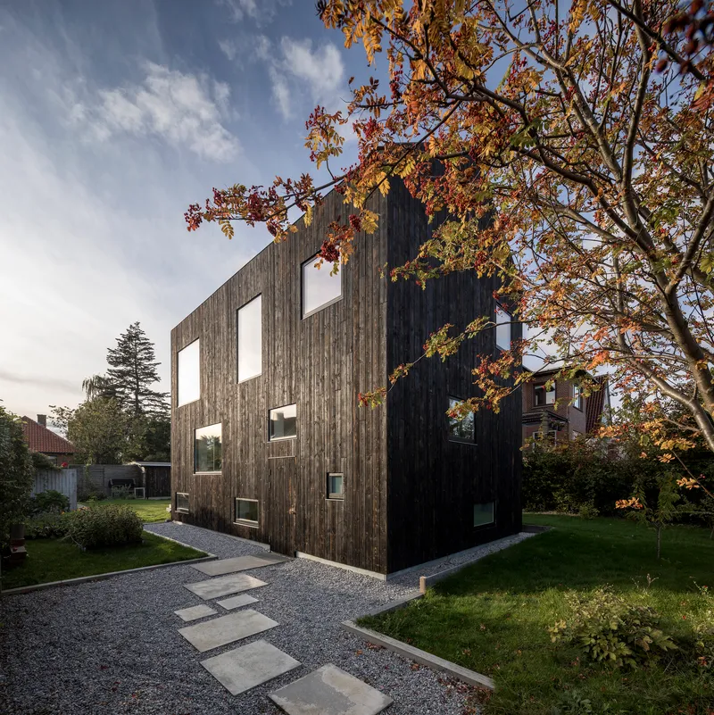Side elevation showing vertically cladded timber volume with scattered window openings framed by autumn branches