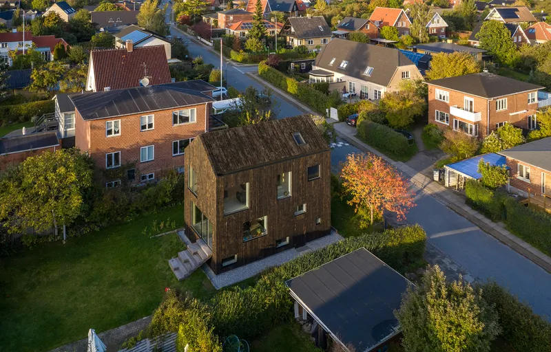 Aerial view of the timber-clad house nestled among neighboring buildings with an autumn tree in front