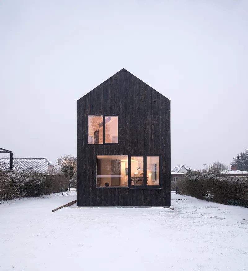 Gable-fronted elevation with charred timber cladding and large glazed openings in a snowy landscape