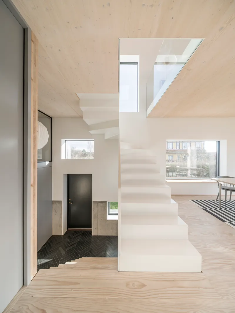 Double-height interior with white folded staircase connecting split levels under a light wood ceiling
