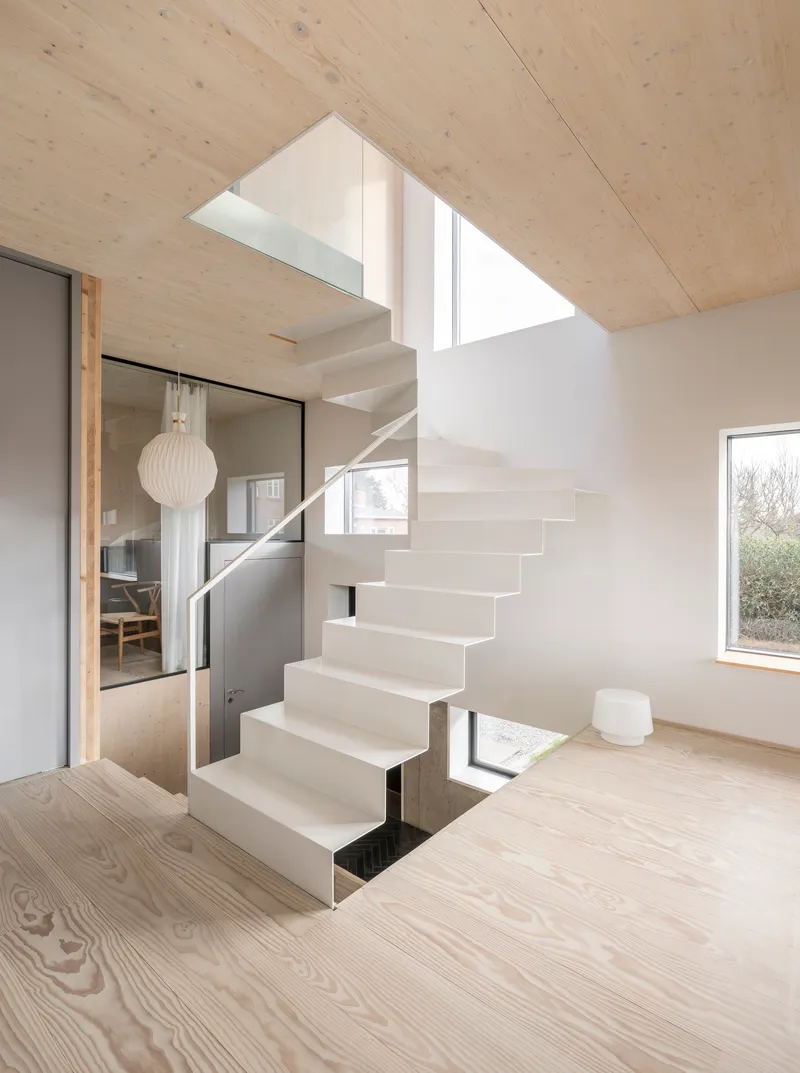 Freestanding white staircase with metal handrail and skylight above in a light wood interior