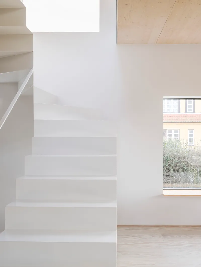 White plastered staircase next to a window overlooking neighboring brick buildings