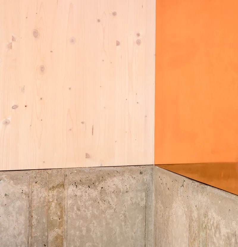 Material junction of light wood paneling, orange wall surface and poured concrete base