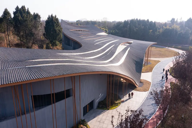 Aerial view of the ribbed metal roof curving between forested hills with visitors on the pathway below