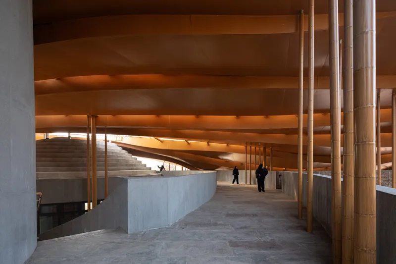 Interior corridor with bamboo columns and illuminated timber ceiling planes framing concrete stairs