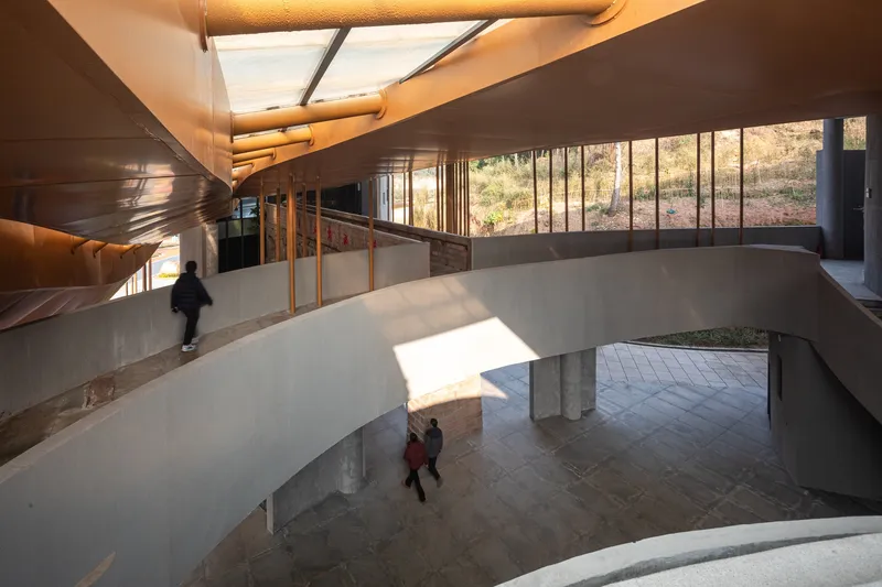 Upper level circulation with ramped concrete floor and glazed wall overlooking lower entrance hall