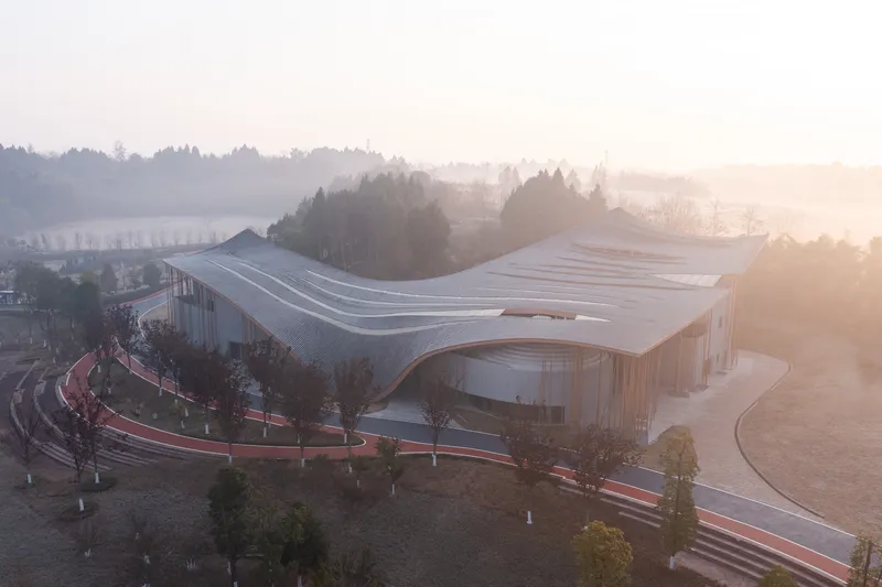 Elevated view of the undulating roof and curving landscape paths at sunrise with distant hills in mist