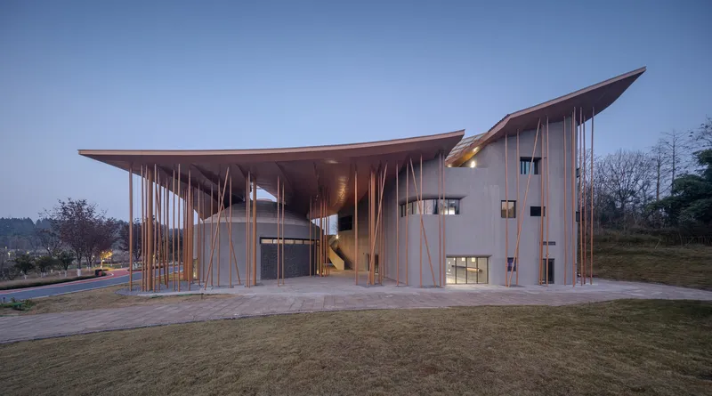 Entrance facade with vertical timber fins and upswept roof edges at dusk with interior lighting visible