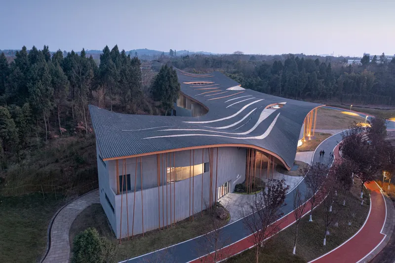 Aerial view of the undulating metal roof with timber cladding at dusk among trees