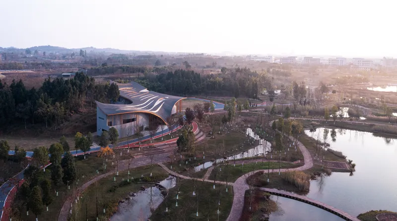 Aerial view of the flowing roof and red pathways winding through planted gardens near water