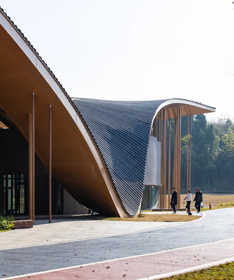 Entrance facade showing the swooping roof soffit and vertical tube screen with visitors walking beneath