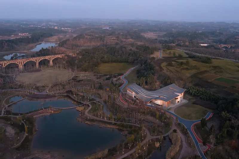 Drone view of the undulating roof building set among pathways and water features at dusk
