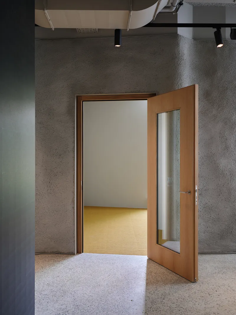 Timber-framed door with narrow glazed panel opening into a yellow-floored room beyond grey textured walls