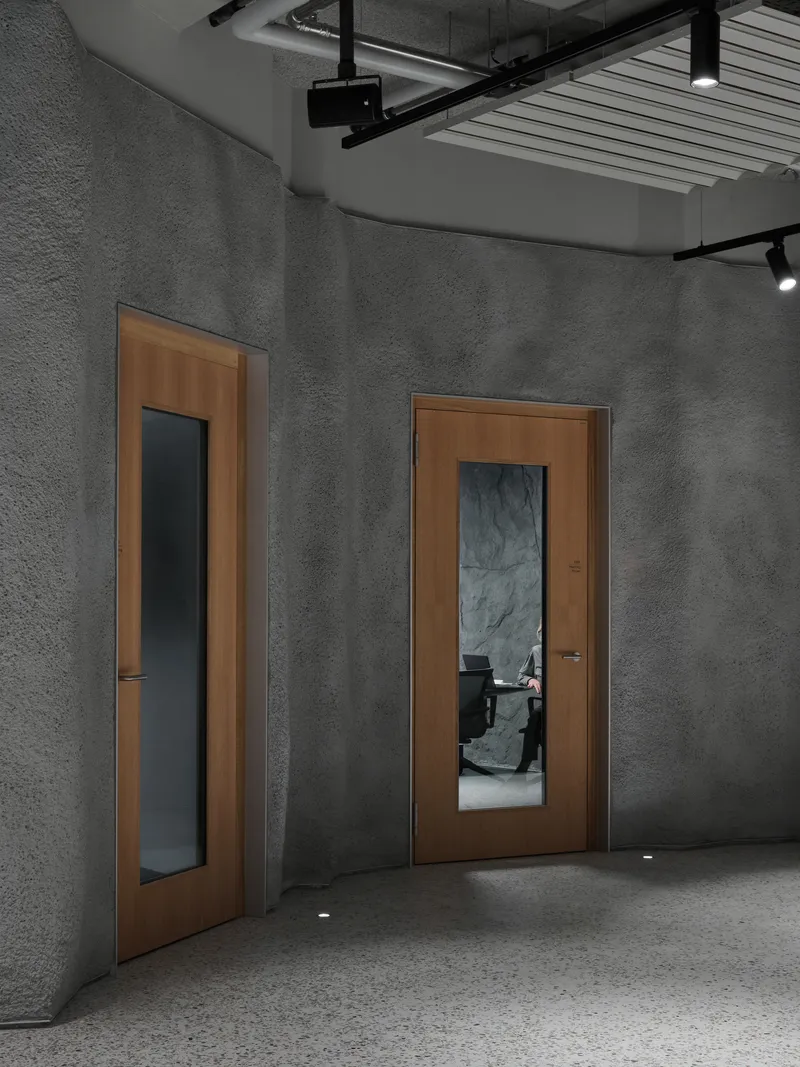 Two timber doors with vertical glazed panels set in grey textured walls under exposed ceiling infrastructure