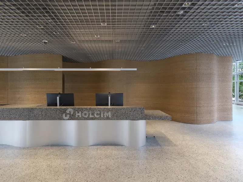 Reception desk with white curved base, terrazzo countertop, and timber wall cladding beneath metal mesh ceiling