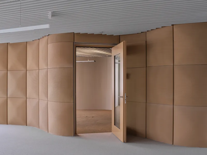 Open double doors in a curved copper-paneled wall revealing an empty room with ribbed ceiling
