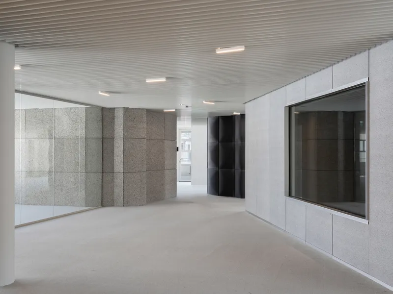 Lobby space with textured grey stone wall panels, black elevator doors, and ribbed metal ceiling with recessed lighting