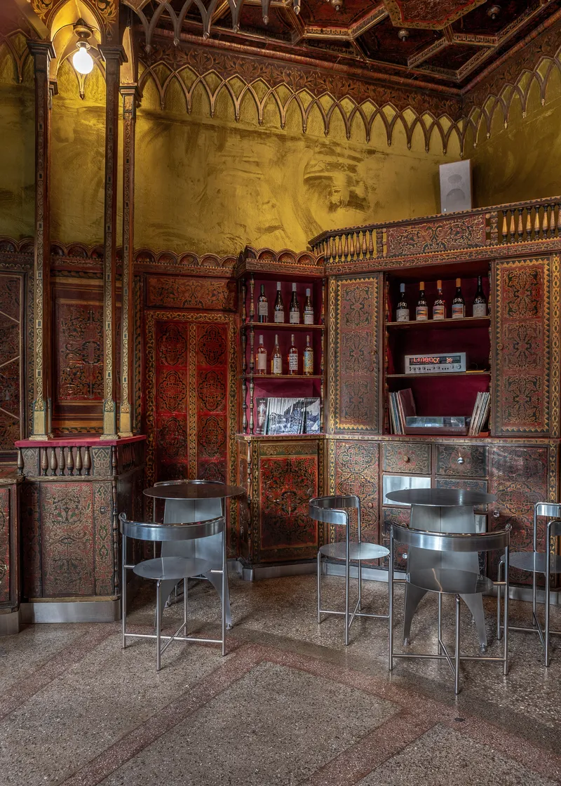 Ornate patterned woodwork surrounding built-in shelving with tubular steel chairs on terrazzo flooring