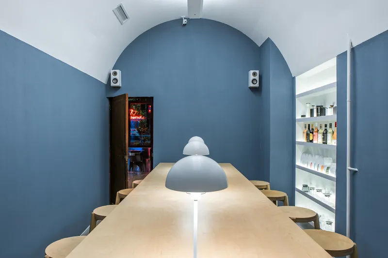 Arched blue wall framing a plywood table with pendant lamp and backlit shelving alcove